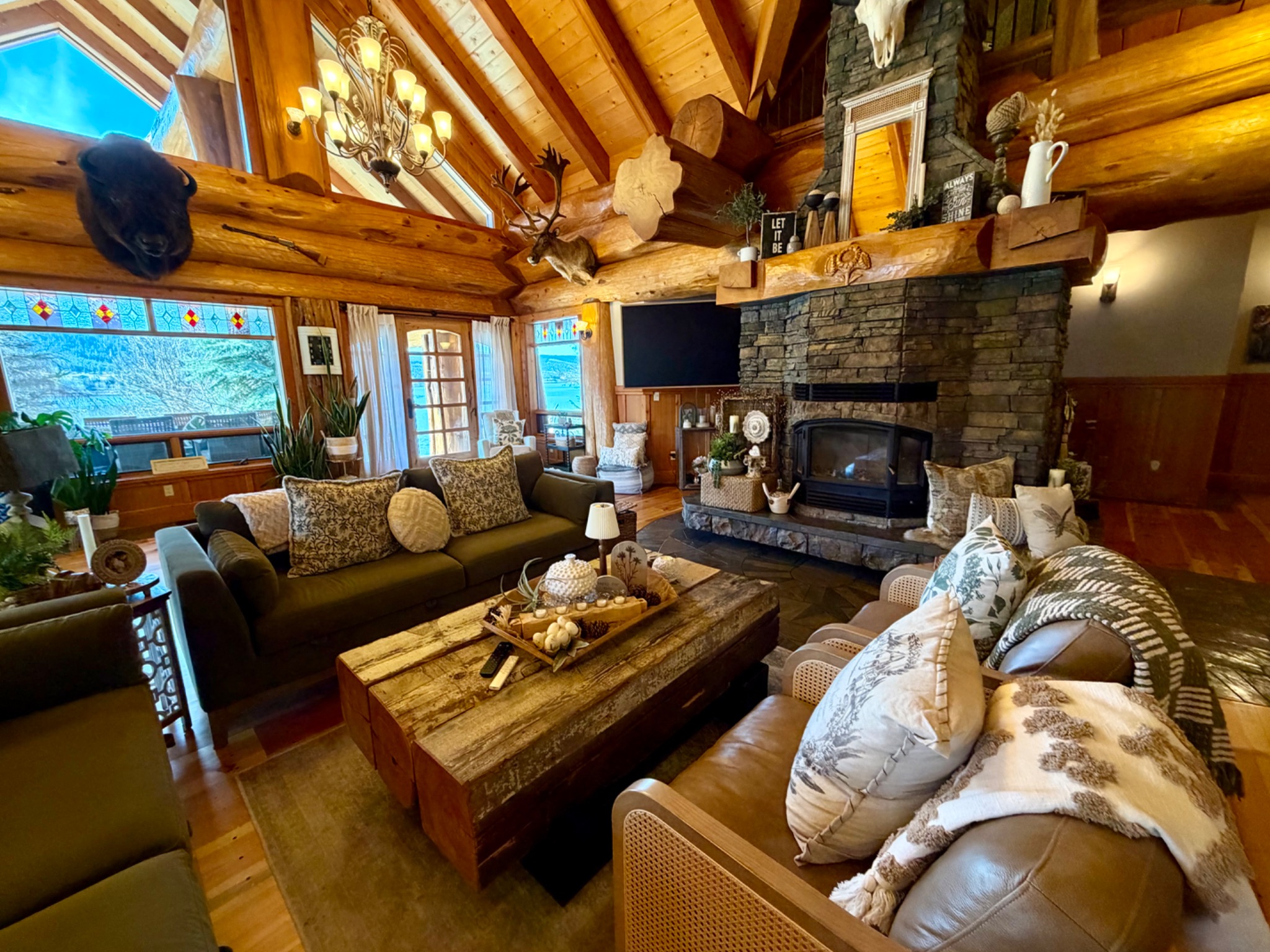 A finished log home great room with a vaulted timber ceiling, stone fireplace and comfortable seating